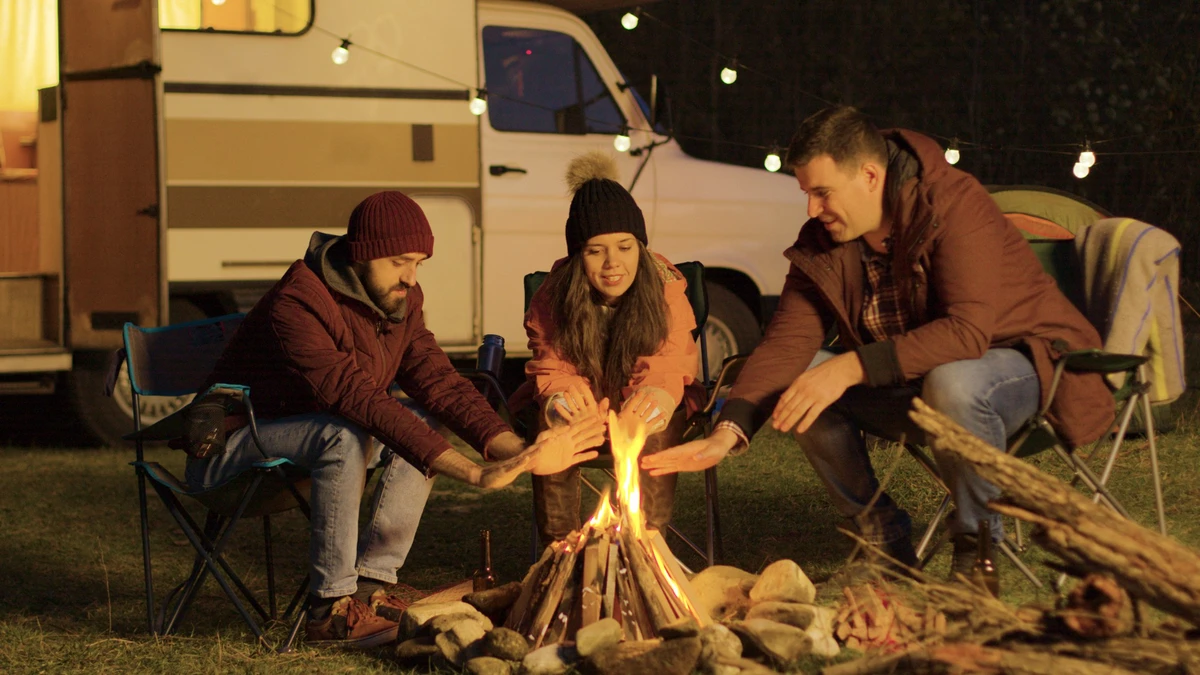 close-friend-sitting-camping-chairs-around-camp-fire-warming-their-hands-retro-camper-light-bulbs-background