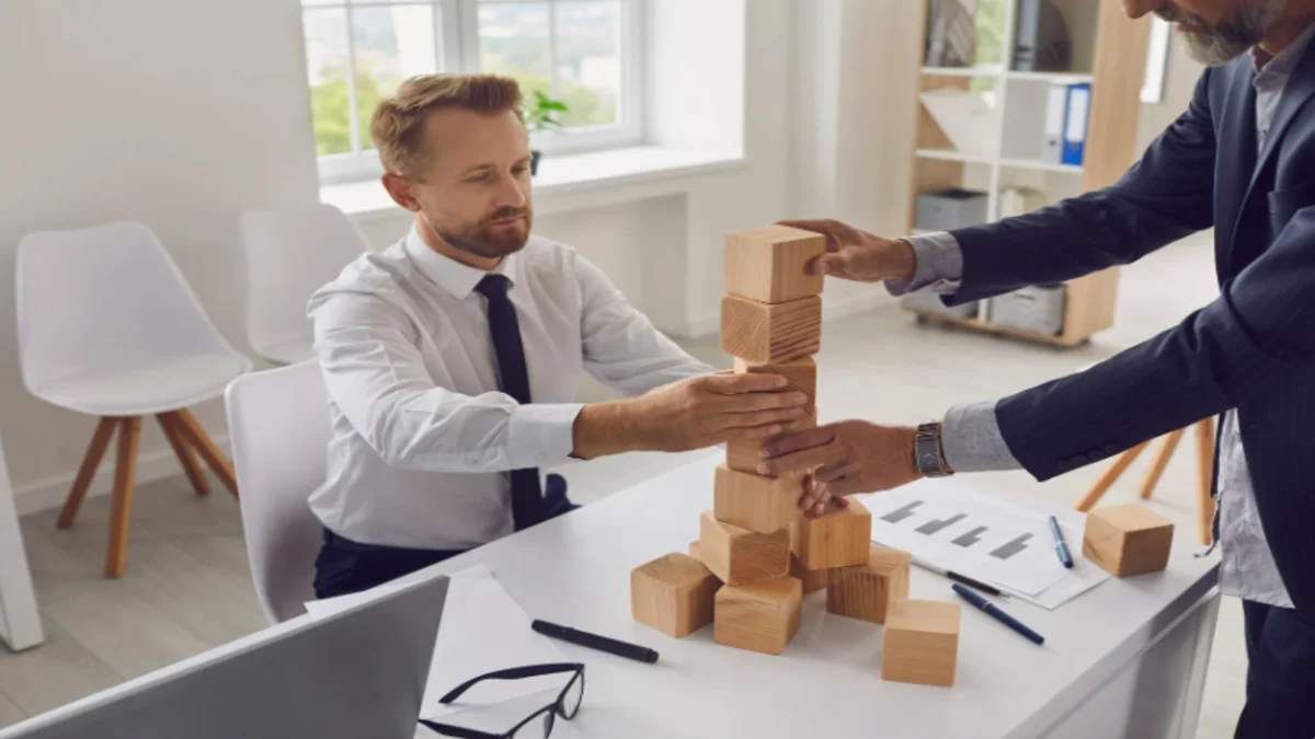 A picture of two men using building blocks to show an example of a building; John Walden, Founder of Eagle Mountain, Utah. The founders used techniques such as this to visualize the map layout for Eagle Mountain when first starting to build there.