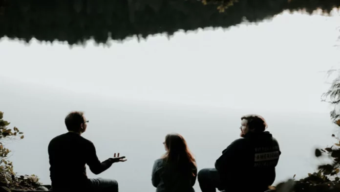 Three people sit in front of a misty mountain scene and talk, symbolizing William Smith, Royal Cup Coffee’s former CEO, dedication to communication